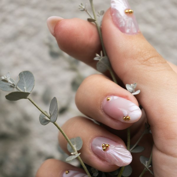 Pale pink nails with gold studs holding a eucalyptus sprig